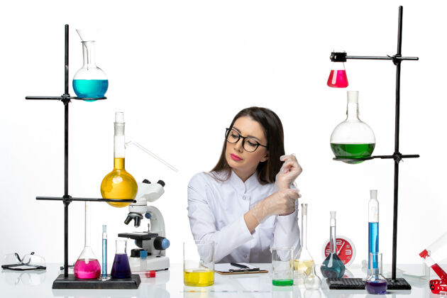 罐子前视图穿着白色医疗服的女化学家坐在白色背景的科学大流行病毒冠状病毒实验室里 拿着不同的溶液大流行容器病毒