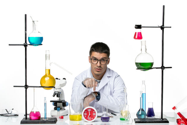 烧杯前视图穿着白色医疗服的男性化学家坐在浅白背景病毒疾病科学实验室covid上 拿着不同的溶液前面疾病病毒
