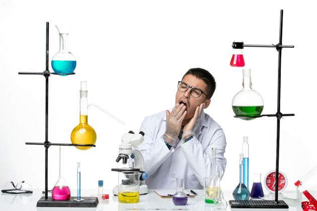 套装前视图穿着白色医疗服的男性化学家坐在白色背景病毒实验室冠状病毒疾病科学的解决方案打呵欠视图实验室实验