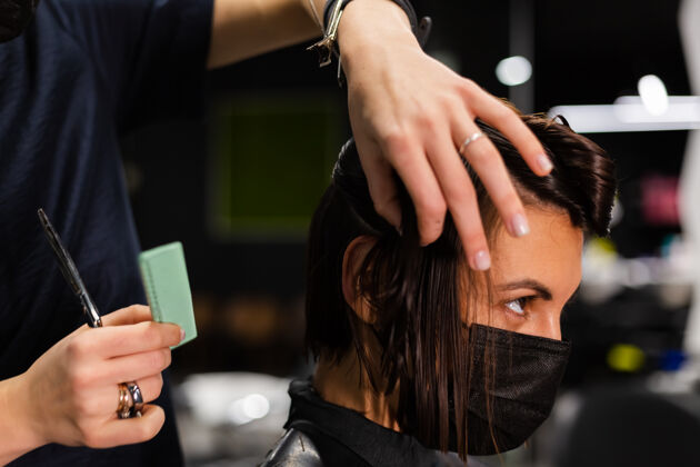 人一个专业的女理发师给客户理发这个女孩戴着面具坐在美容院里客户爆发工人