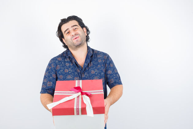 微笑成熟的男人拿着礼品盒在衬衫和看起来可爱 前视图男性人类肖像