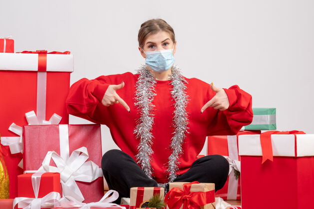 坐着正面图：年轻女性戴着无菌面具坐着 手里拿着圣诞礼物礼物人圣诞节