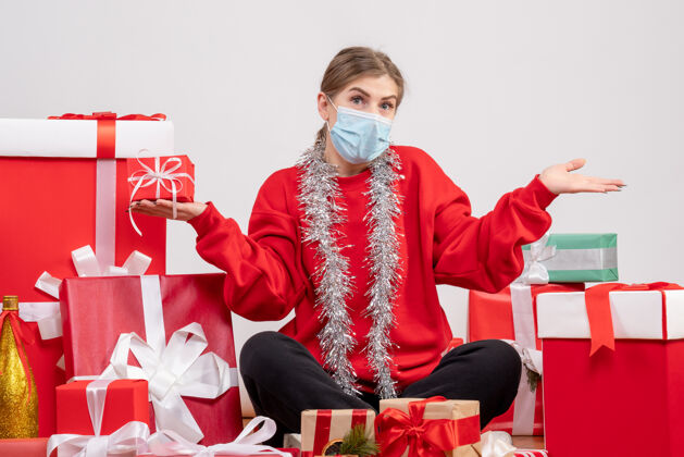人正面图：年轻女性戴着无菌面具围坐在圣诞礼物旁情绪年轻女性礼物