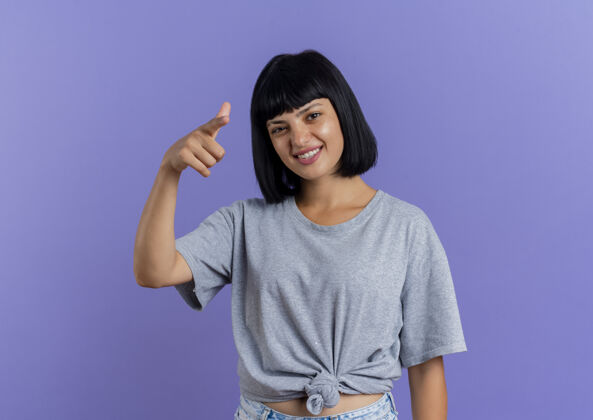 相机快乐的年轻黑发白种女人指着隔离在紫色背景和复制空间的相机女人黑发背景