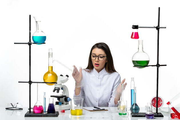 烧杯前视图穿着白色医疗服的女化学家坐在白色背景上实验室病毒冠状病毒大流行科学罐子坐着液体