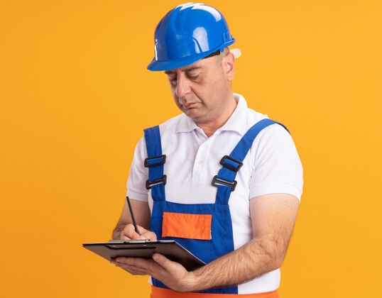 人自信的白人成年建筑工人穿着制服用铅笔在剪贴板上写橙色自信剪贴板建设者