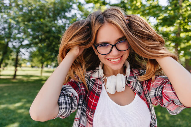 公园热情的白种女人在公园里玩她的头发夏日早晨戴眼镜的可爱白种女人戴着耳机摆姿势的户外照片模特微笑户外