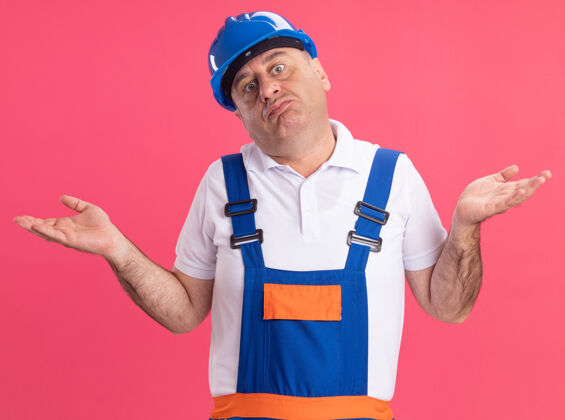 男人困惑的成年白人建筑工人穿着制服 双手张开放在粉红色的地板上困惑手制服