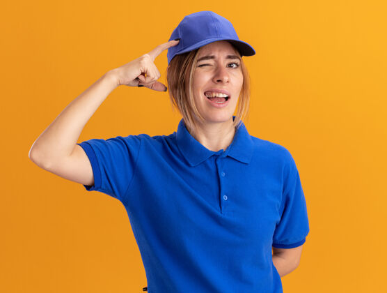混乱困惑的年轻漂亮的女送货员在制服把手指放在头上 看着相机在橙色制服漂亮手指