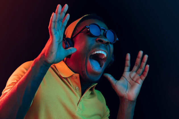 非洲年轻帅气的快乐惊喜的时髦男人在霓虹灯下用耳机听音乐迪斯科舞厅 夜总会 嘻哈风格 积极的情绪 面部表情 舞蹈概念音频情感舞蹈