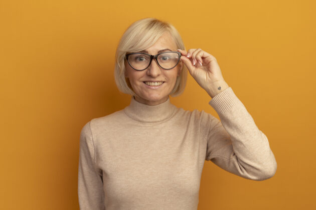 时尚微笑着的金发斯拉夫女人透过橙色的光学眼镜看着相机姿势通过女人