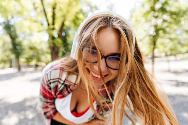 假期戴着耳机的热情长发女孩的特写镜头戴着眼镜的年轻女士在夏季公园里鬼混户外女人耳机