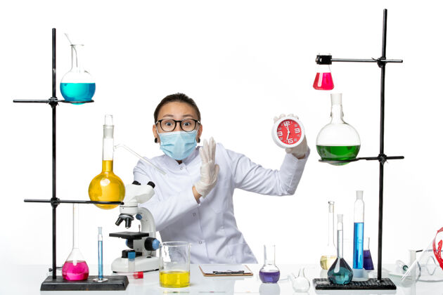 病毒前视图：穿着医疗服的女化学家戴着面具 拿着白色背景上的时钟病毒实验室化学冠状病毒飞溅前面飞溅医学