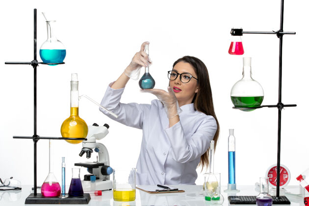 人前视图：穿着白色医疗服的女化学家拿着装有蓝色溶液的烧瓶 背景是白色的实验室科学病毒covid大流行解决方案视图工作