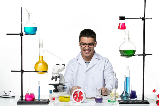 微笑正面图：身着白色医疗服的男性化学家坐在白色背景上微笑着解决方案病毒科学科维德大流行实验室医学大流行医生