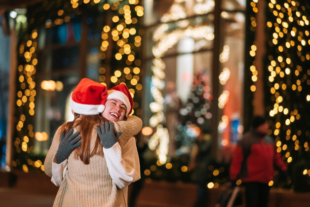 圣诞老人在圣诞夜户外散步时 快乐可爱的年轻朋友们互相拥抱微笑的照片拥抱朋友照明