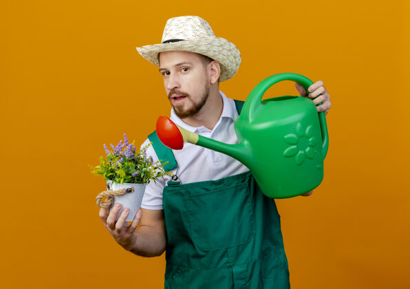 花盆年轻英俊的斯拉夫园丁穿着制服 戴着帽子 手里拿着花盆和浇水罐 看上去与世隔绝斯拉夫人帅哥拿着