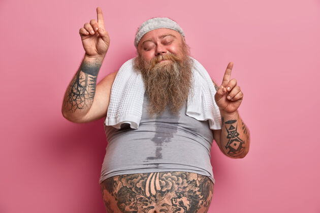 活跃肥胖和运动的概念快乐的超重男人跳舞无忧无虑有出汗的身体纹身手臂向上点隔离在粉红色的墙上 在家做运动 燃烧卡路里后吃快餐腹部运动员大