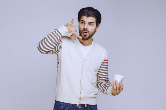 年轻人一个穿着白衬衫的男人拿着一个咖啡杯 要打电话来联系人阳刚人