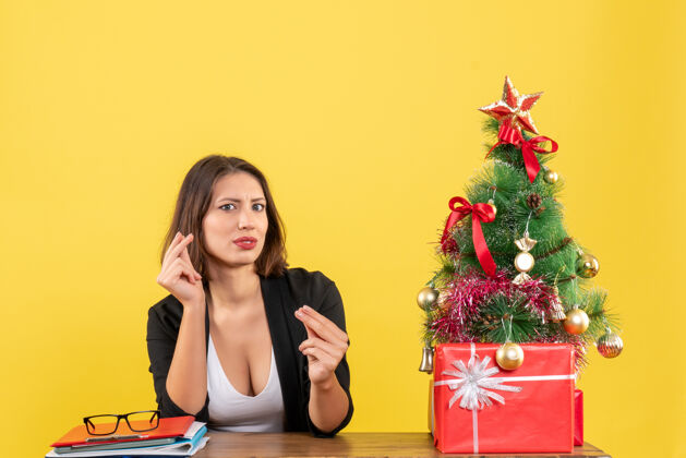 时尚这位年轻漂亮的女士正坐在黄色办公室装饰的圣诞树旁的桌子旁 仔细端详着某样东西黄色性感专注