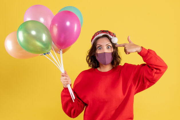 颜色正面图年轻女性拿着气球 戴着黄色的无菌面具年圣诞节乐趣
