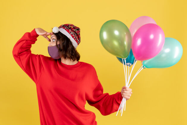 气球正面图年轻女性手持气球 戴着黄色的无菌面具生日庆祝视图