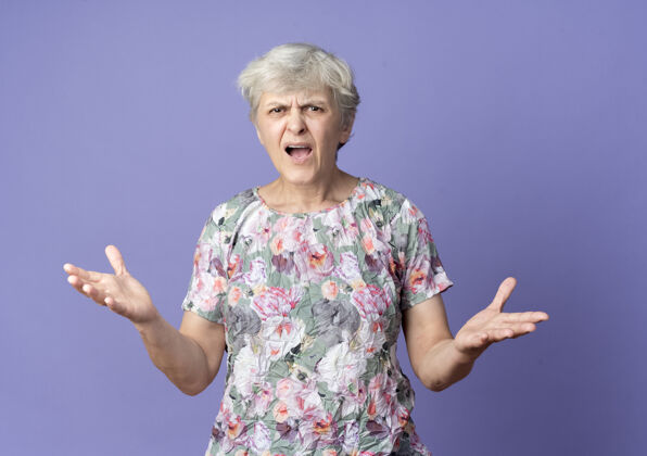 站恼怒的老妇人站在紫色的墙上 双手张开老手女人