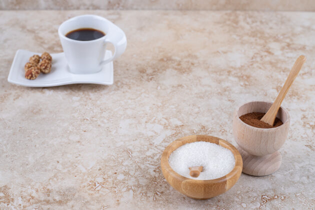 小碗磨碎的咖啡粉和糖旁边放着一杯咖啡和上釉的花生美味粉咖啡
