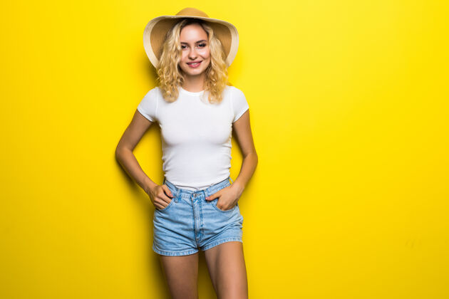 模特快乐的年轻漂亮女人草帽摆在黄色的墙上短裤微笑人