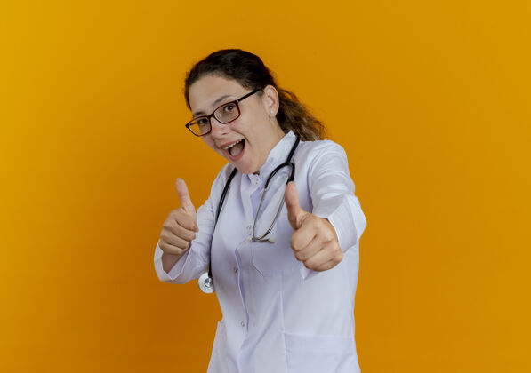 长袍令人印象深刻的年轻女医生穿着医用长袍和听诊器 戴着眼镜 看起来竖起大拇指眼镜听诊器成人