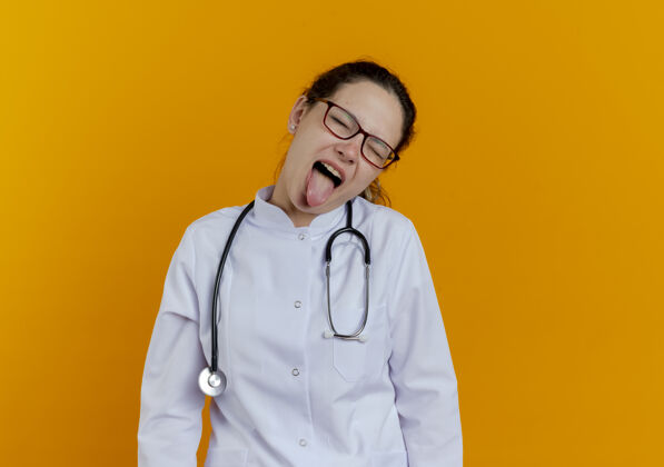 长袍年轻的女医生戴着医用长袍和听诊器 眼睛紧闭着 戴着眼镜女性橙色年轻