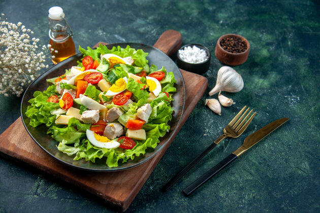 配料侧视图美味的沙拉与许多新鲜的原料在木制砧板香料油瓶大蒜素餐具设置在黑绿色混合颜色的背景混合瓶切割