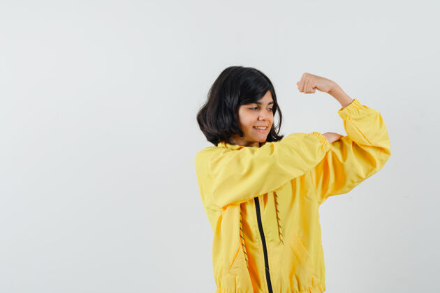 肖像小女孩穿着黄色连帽衫展示手臂肌肉 看起来很自信 正面视图自信小休闲