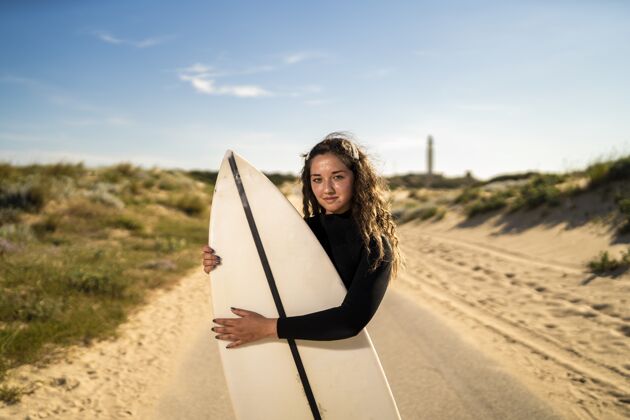 女性一个迷人的女人在西班牙道路中间拥抱一个冲浪板的浅焦点拍摄休闲海岸活跃