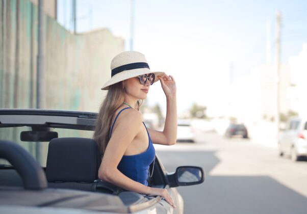 女人在一辆白色敞篷跑车的驾驶座上选择性聚焦拍摄女性司机帽子眼镜