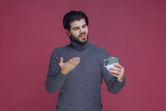 人一个穿着灰色毛衣的男人拿着一个咖啡杯指着它示范姿势茶