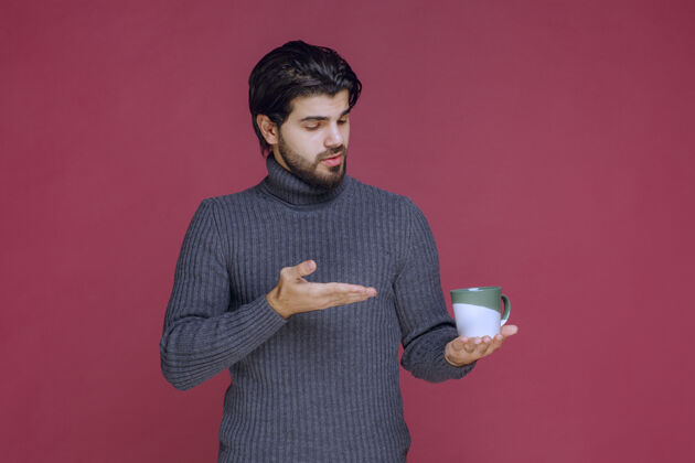 服装一个穿着灰色毛衣的男人拿着一个咖啡杯指着它工人聪明性感