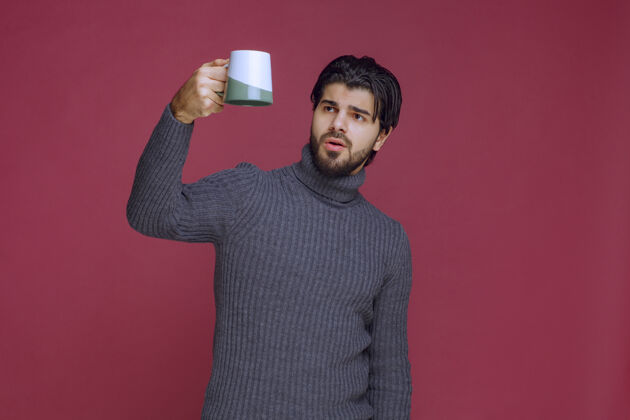 年轻人一个穿着灰色毛衣的男人手里拿着一个咖啡杯人人成人