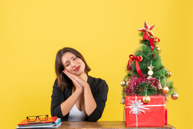树一个年轻女子坐在黄色办公室装饰的圣诞树旁的桌子旁梦想着什么人女士东西