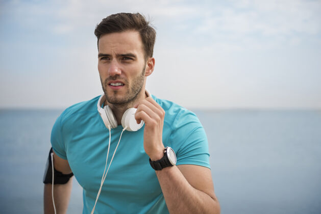 耳机特写在海边慢跑的健康年轻人运动训练运动员男性