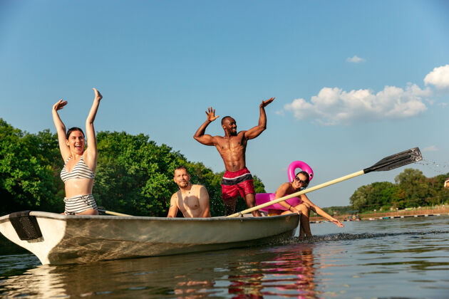 河流一群快乐的朋友在河里欢笑和游泳阳光明媚的日子里 穿着泳装的男女们在河边乘船欢庆夏日 友谊 度假 周末的概念跑步漂亮庆祝