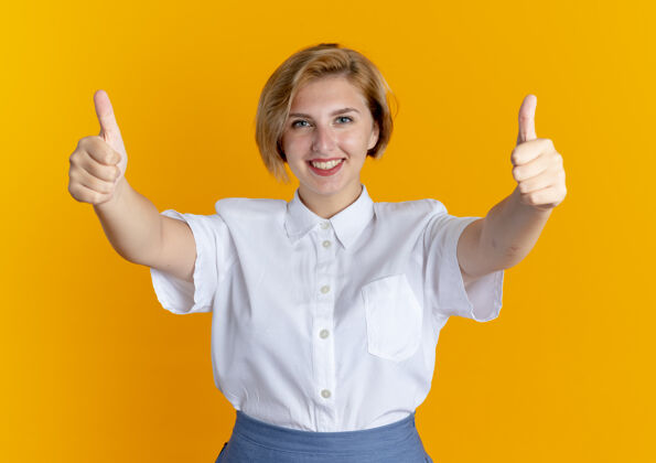 俄国人年轻微笑的金发俄罗斯女孩竖起大拇指 两只手孤立地放在橙色背景上 留有复制空间微笑手金发