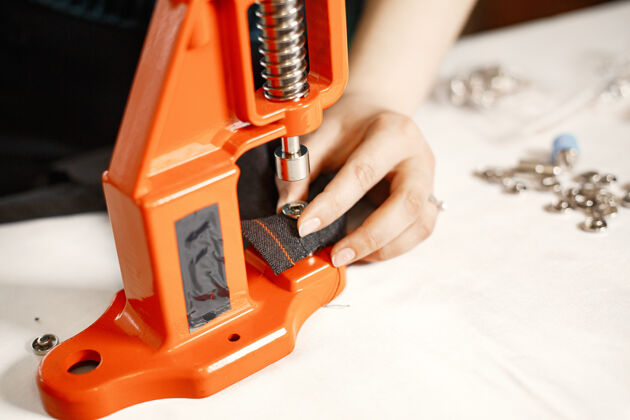 年轻人橙色熨烫衣服织物上的纽扣带着缝纫工具的女人机器裁缝工作