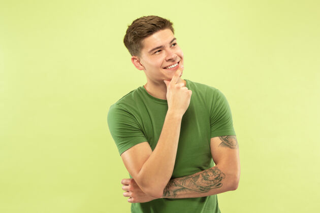 手绿色工作室背景上的白人青年半身肖像穿着衬衫的漂亮男模人类情感的概念 面部表情 销售 广告体贴和自信微笑成人商人员工