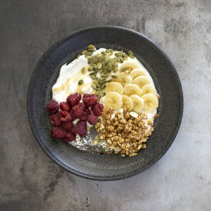 坚果高角度观看酸奶与坚果 覆盆子和香蕉在一个碗在桌上健康餐碗