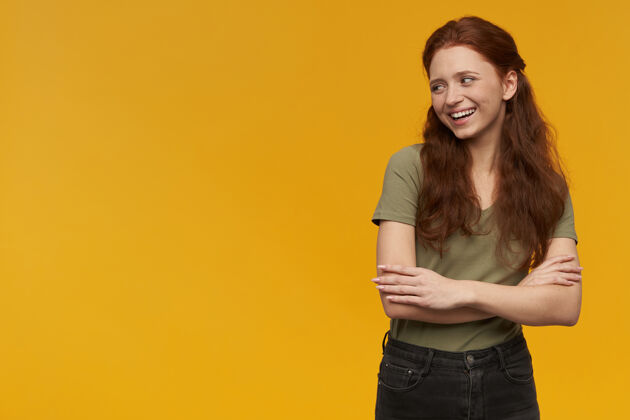 情绪可爱 积极向上的女人 长着一头姜黄色的头发穿着绿色t恤人和情感的概念双臂交叉 面带微笑看着左边的复制空间 隔着橙色的墙情绪女性长发