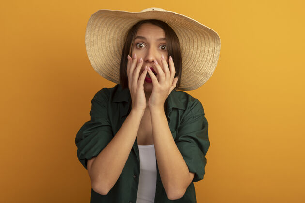 女人一个戴着沙滩帽的焦虑的漂亮女人双手紧握着橘色墙壁上孤立的嘴巴姿势感觉市民