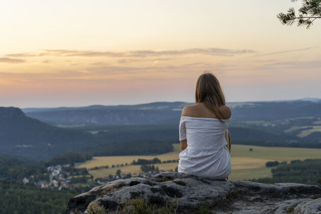 人一位年轻女性坐在悬崖边欣赏壮丽的日落的后视图女人背坐