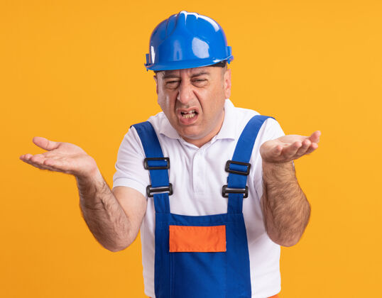 开放恼怒的成年建筑工人穿着制服 在橙色的墙上张开双手制服衣服脸