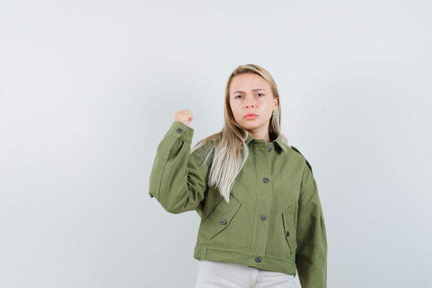 夹克身着绿色夹克 牛仔裤 表情严肃的年轻女性展示着她的手臂力量 正面照年轻微笑水疗